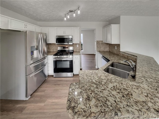 kitchen with light wood finished floors, decorative backsplash, appliances with stainless steel finishes, a sink, and light stone countertops