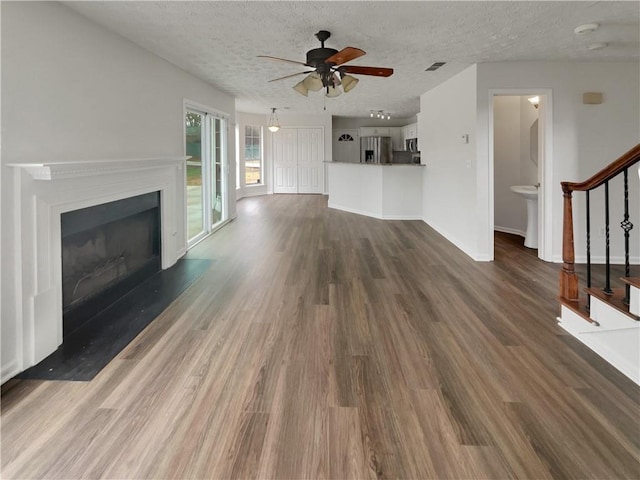 unfurnished living room with a textured ceiling, a fireplace with raised hearth, visible vents, stairway, and dark wood finished floors