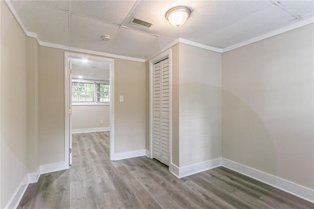 unfurnished bedroom featuring wood finished floors, a closet, baseboards, and ornamental molding