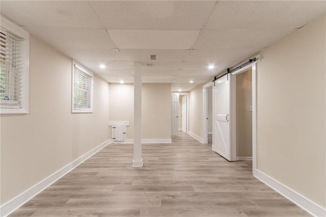 basement featuring light wood-type flooring, a barn door, baseboards, a paneled ceiling, and recessed lighting