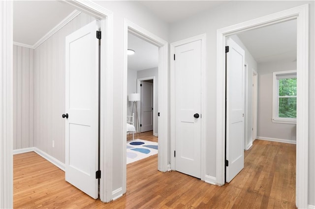 corridor with ornamental molding and light hardwood / wood-style floors