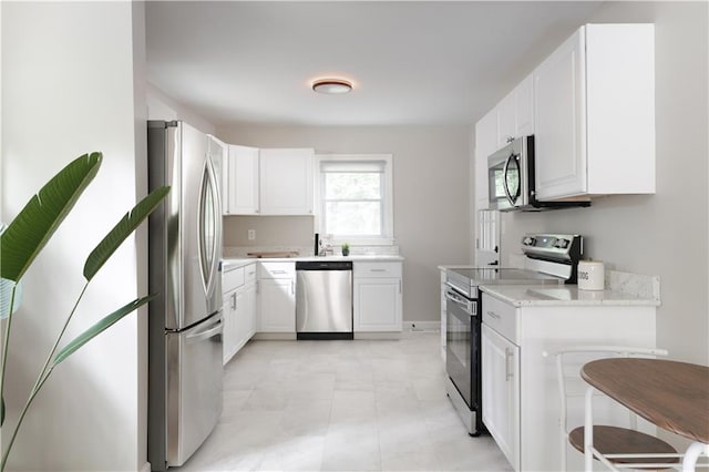 kitchen featuring light stone countertops, white cabinetry, appliances with stainless steel finishes, and a kitchen breakfast bar