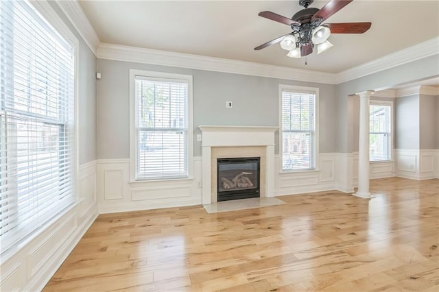 unfurnished living room with a healthy amount of sunlight, a wainscoted wall, light wood finished floors, and decorative columns