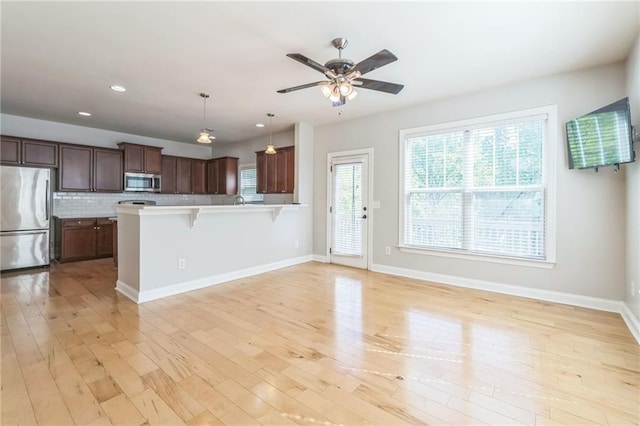 kitchen with stainless steel appliances, light countertops, backsplash, light wood-type flooring, and a breakfast bar area