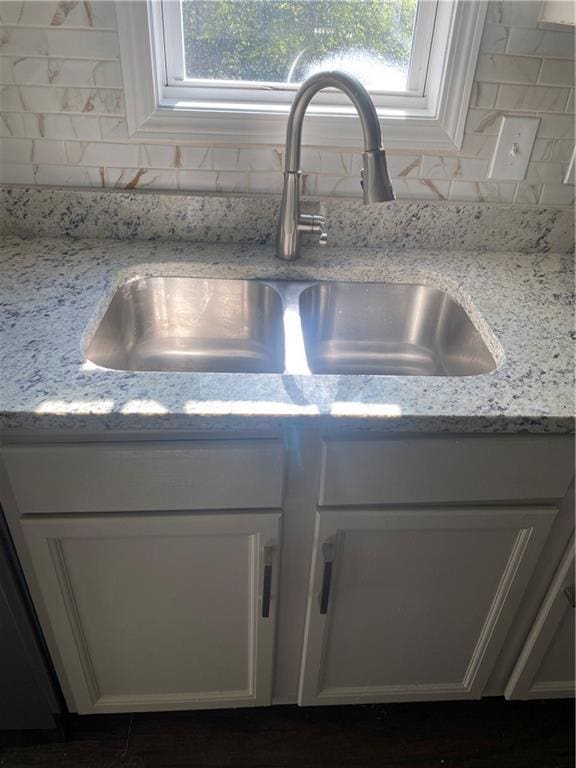 details with decorative backsplash, light stone counters, white cabinetry, and sink