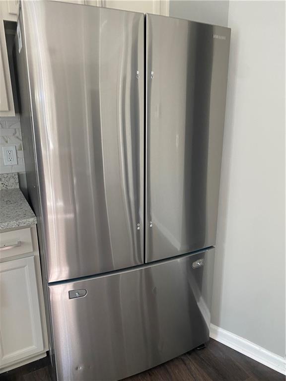 room details featuring stainless steel refrigerator, white cabinetry, light stone countertops, and dark hardwood / wood-style floors