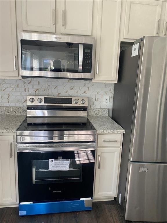 kitchen with white cabinets, stainless steel appliances, light stone counters, and dark wood-type flooring