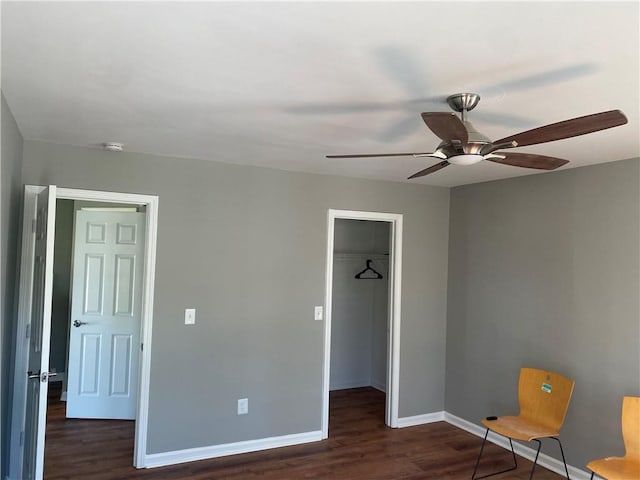 unfurnished bedroom with a walk in closet, ceiling fan, a closet, and dark hardwood / wood-style floors