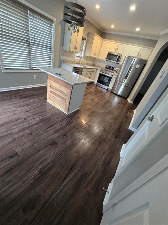 kitchen featuring white cabinetry, light stone countertops, crown molding, pendant lighting, and appliances with stainless steel finishes