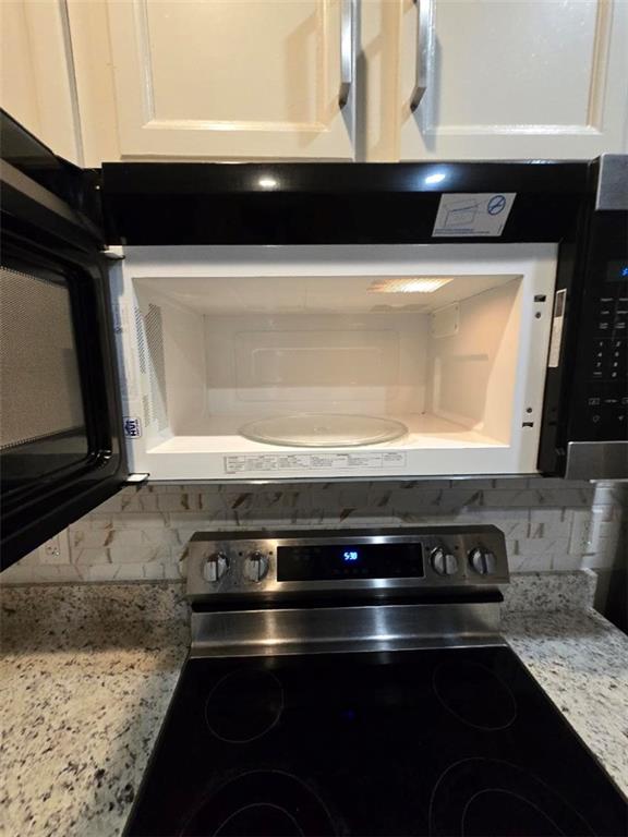 interior details with electric range, light stone counters, white cabinetry, and backsplash