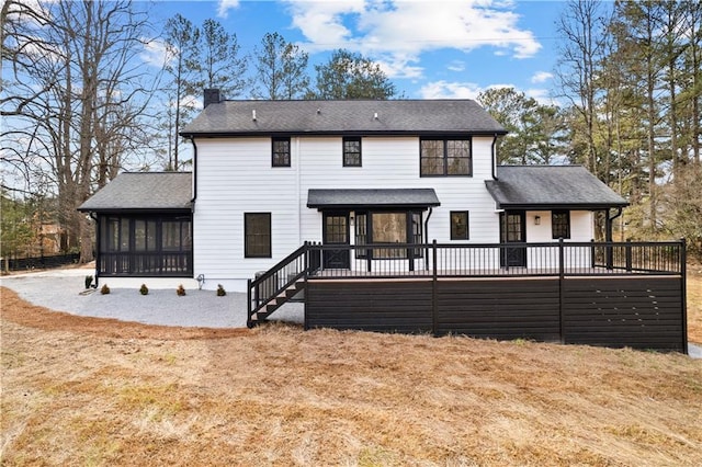 rear view of house featuring a deck, a sunroom, roof with shingles, and a chimney