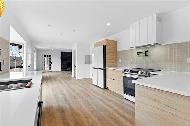 kitchen with freestanding refrigerator, stainless steel electric stove, light wood-style floors, premium range hood, and a fireplace