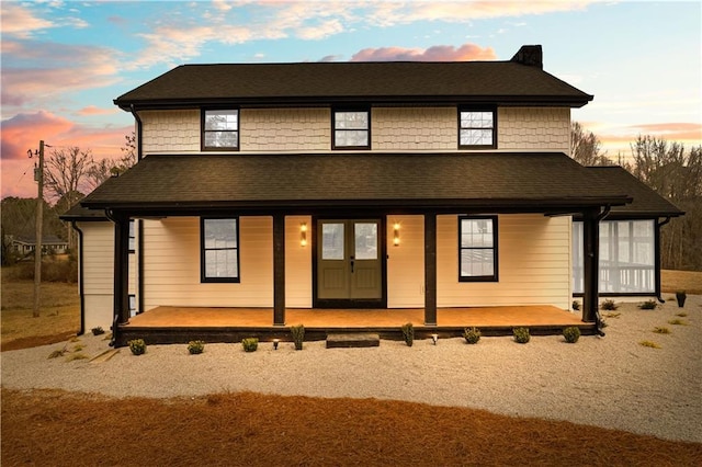 back of property at dusk featuring a shingled roof and a porch