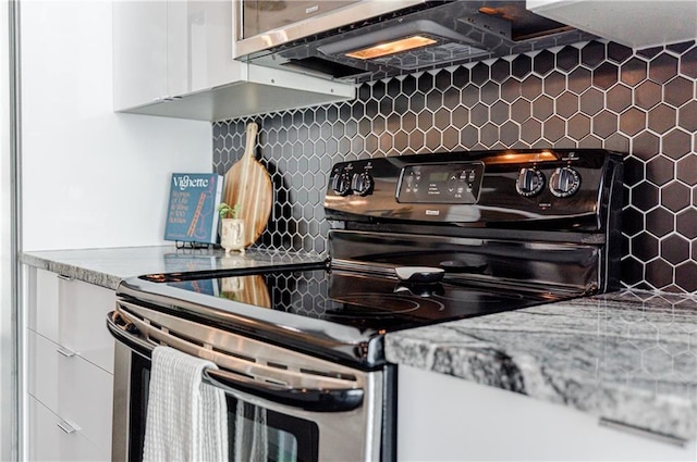 kitchen with light stone countertops, stainless steel electric range, white cabinets, and backsplash