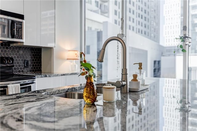 room details with tasteful backsplash, stone countertops, white cabinets, modern cabinets, and appliances with stainless steel finishes