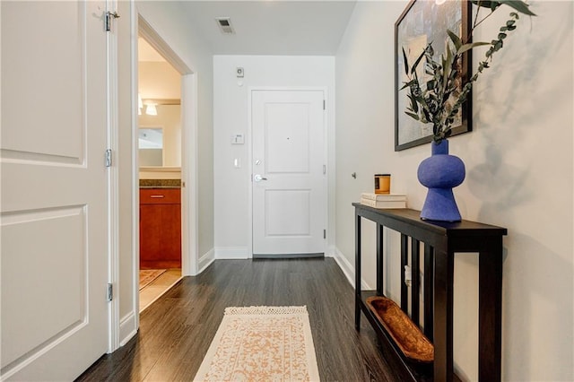 hall with dark wood-type flooring, visible vents, and baseboards