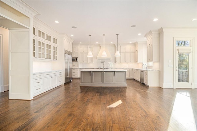 kitchen featuring a center island with sink, white cabinets, hanging light fixtures, built in appliances, and tasteful backsplash