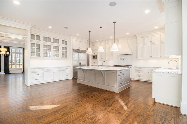 kitchen featuring premium range hood, built in appliances, an island with sink, a breakfast bar area, and white cabinets