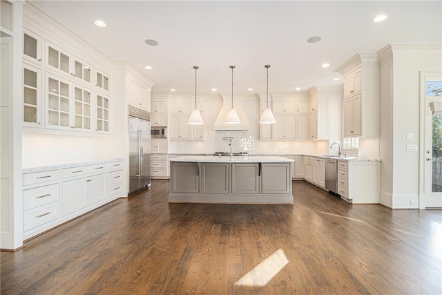 kitchen with built in appliances, white cabinets, a center island with sink, and hanging light fixtures