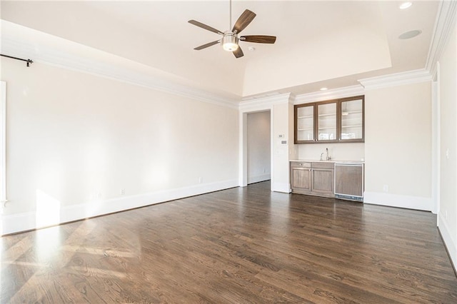 unfurnished living room featuring dark wood-type flooring, sink, crown molding, ceiling fan, and a tray ceiling