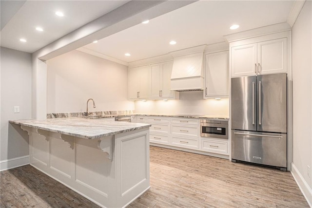 kitchen with kitchen peninsula, white cabinetry, custom exhaust hood, and appliances with stainless steel finishes