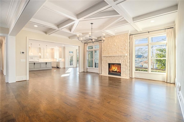 unfurnished living room with coffered ceiling, dark wood-type flooring, beam ceiling, an inviting chandelier, and a fireplace