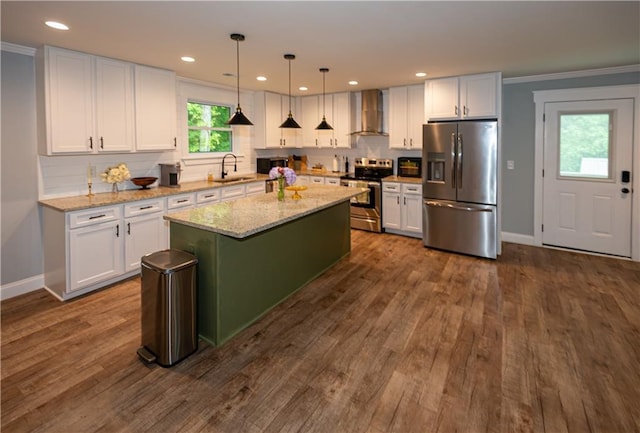 kitchen with appliances with stainless steel finishes, white cabinetry, a sink, baseboards, and wall chimney exhaust hood