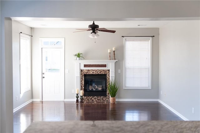 unfurnished living room with ceiling fan, a fireplace, baseboards, and wood finished floors