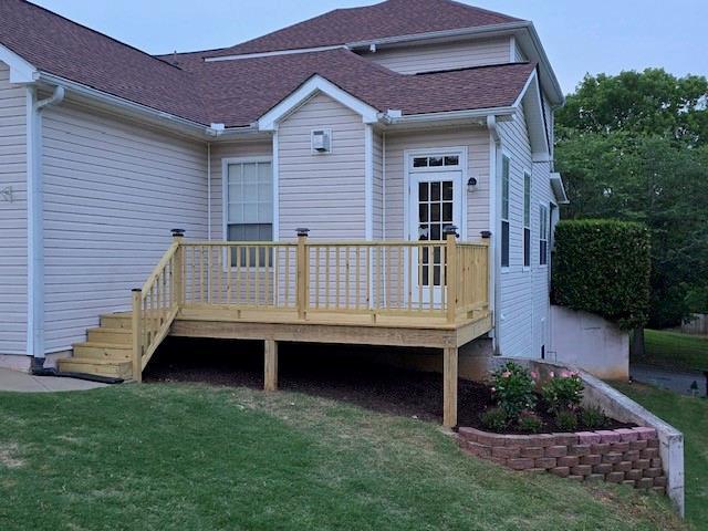 back of property with a deck, roof with shingles, and a lawn