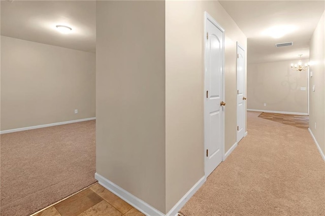 hall featuring an inviting chandelier and light colored carpet