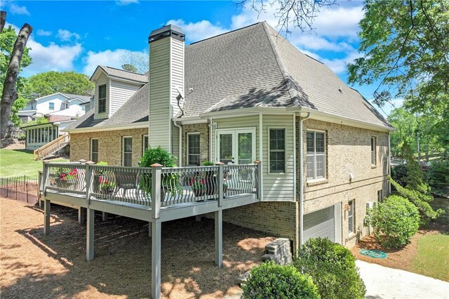 back of house featuring brick siding, a chimney, a garage, and a deck