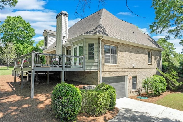 rear view of property with concrete driveway, an attached garage, brick siding, and a wooden deck