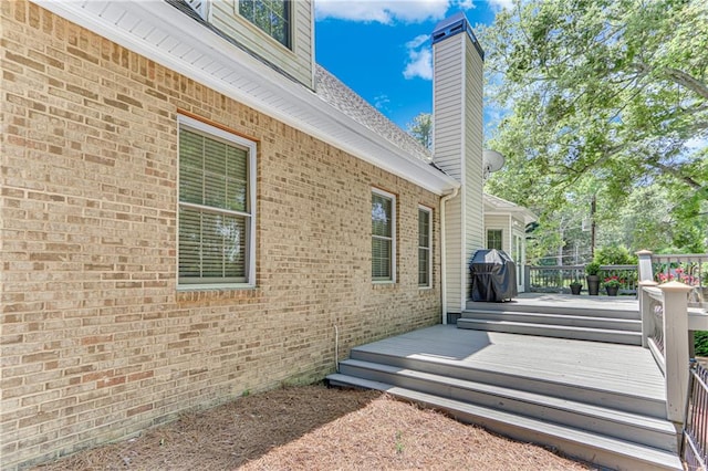 view of side of home featuring a chimney, a wooden deck, brick siding, and roof with shingles