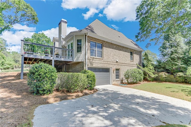 rear view of property with a chimney, concrete driveway, a wooden deck, brick siding, and an attached garage