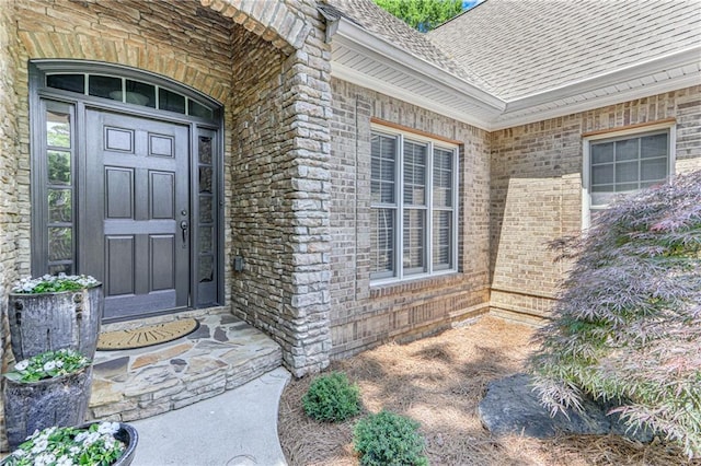 doorway to property featuring brick siding and roof with shingles