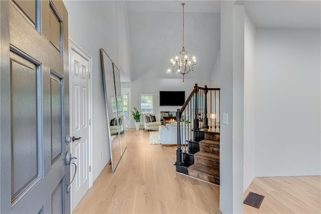 entryway with high vaulted ceiling, stairs, light wood finished floors, a notable chandelier, and visible vents