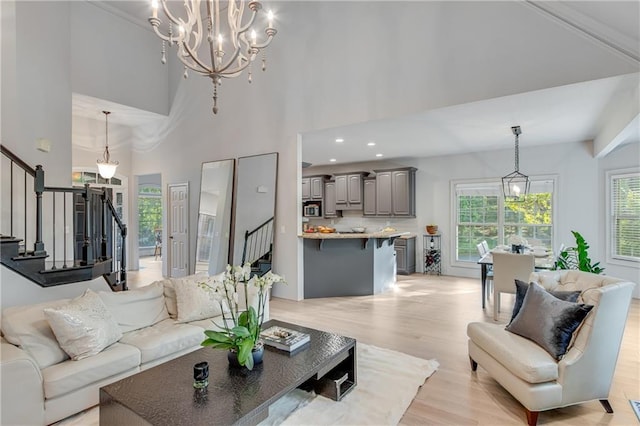 living room with stairway, an inviting chandelier, a towering ceiling, and light wood-style flooring