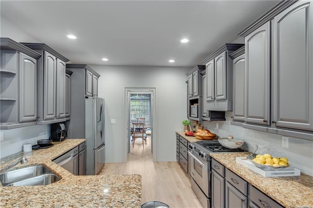 kitchen featuring open shelves, appliances with stainless steel finishes, a sink, and gray cabinetry