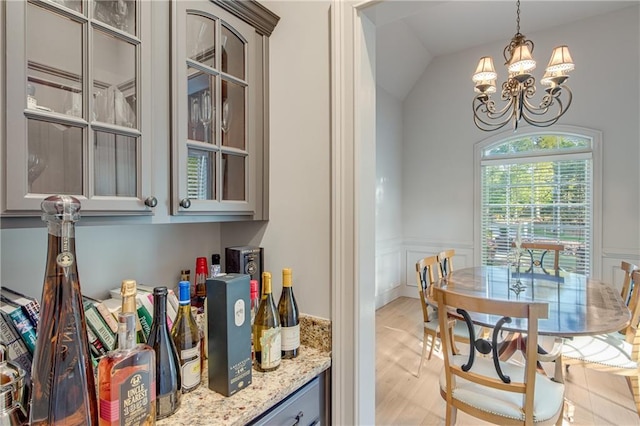 interior space with wainscoting, light wood-style floors, a chandelier, lofted ceiling, and hanging light fixtures