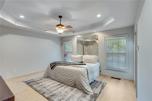 bedroom featuring ceiling fan, ornamental molding, a tray ceiling, and light wood-style flooring