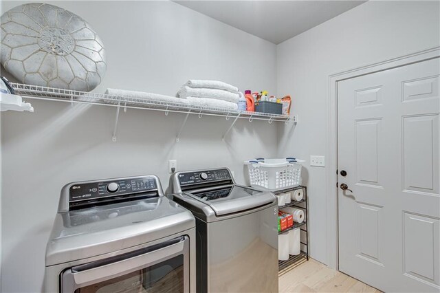 clothes washing area with independent washer and dryer, light wood-style floors, and laundry area
