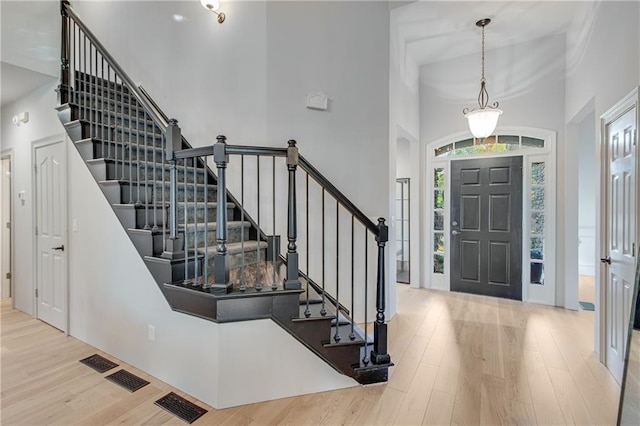 entrance foyer featuring stairs, visible vents, wood finished floors, and a high ceiling