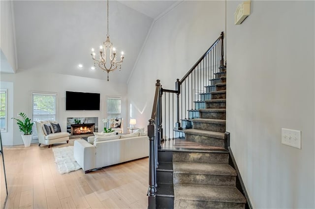stairs with an inviting chandelier, wood finished floors, ornamental molding, a premium fireplace, and high vaulted ceiling