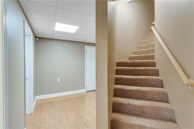 stairs featuring wood finished floors, a drop ceiling, and baseboards