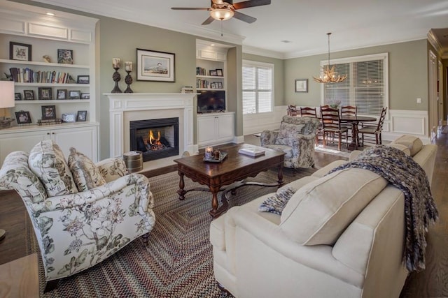 living room featuring crown molding, built in features, and ceiling fan with notable chandelier