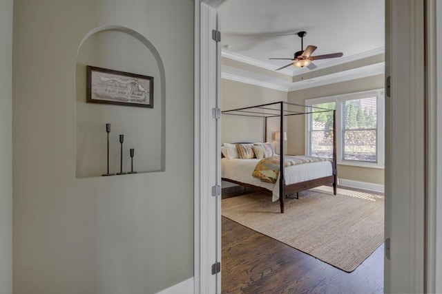 bedroom with ceiling fan, dark hardwood / wood-style flooring, crown molding, and a tray ceiling