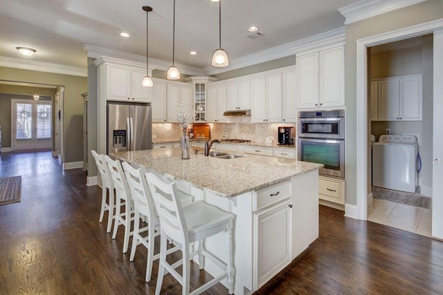 kitchen with a center island with sink, white cabinets, appliances with stainless steel finishes, tasteful backsplash, and washer / clothes dryer