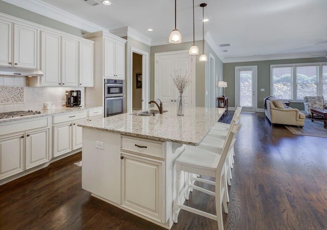 kitchen with appliances with stainless steel finishes, tasteful backsplash, sink, decorative light fixtures, and a center island with sink