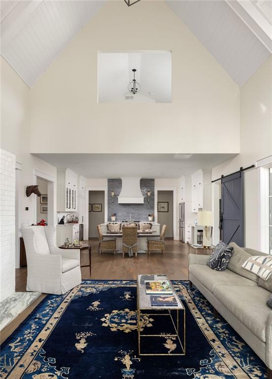 9229 Selborne Ln, Chattahoochee Hills, GA 30268 - living area with high vaulted ceiling, a barn door, wood finished floors, and beamed ceiling