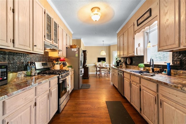kitchen with appliances with stainless steel finishes, a sink, tasteful backsplash, under cabinet range hood, and ornamental molding